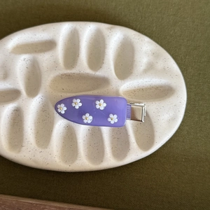 Dettaglio molletta per capelli viola con margherite bianche su un vassoio di ceramica