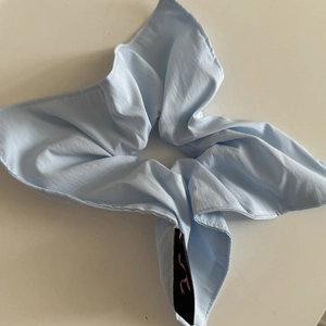 Minimalist light blue scrunchie hair accessory with smooth fabric and black woven label