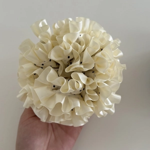 Close-up of cream satin scrunchie with delicate black polka dots and pleated texture