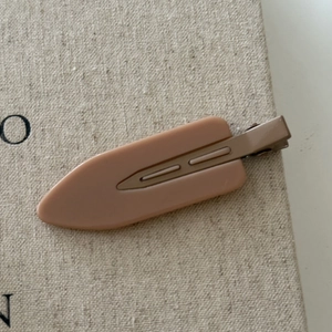 Close-up of a large matte pink seamless duckbill hair clip on textured beige fabric