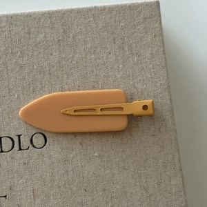 Close-up of matte apricot duckbill hair clip with metal base on textured background