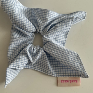 Detailed view of blue gingham hair scrunchie with a pink hand made label and cotton texture