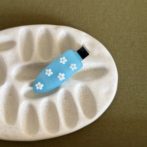 Dettaglio del fermaglio per capelli in acrilico azzurro con cinque fiori di plumeria