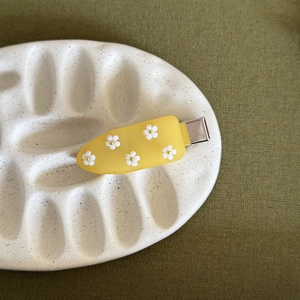 Dettaglio ravvicinato di un fermaglio giallo in acrilico con piccoli fiori di frangipane