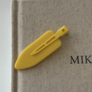 Detail view of yellow surfboard hair clip with matte finish and metal duckbill clip