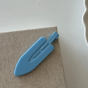 Close-up of light blue matte hair clip with flat paddle design on a textured beige fabric