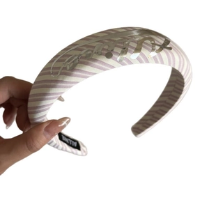 Handheld view of a wide purple and white striped headband with silver metallic letters
