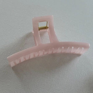Close-up of a light pink jelly-colored hair claw clip with golden metal spring detail