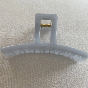 Detailed top view of a light gray jelly resin hair claw clip with a golden metal spring