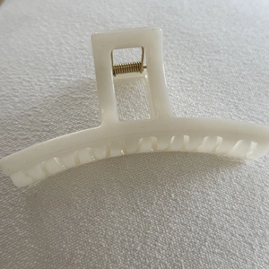 Close-up of cream white hair claw clip with golden metal spring on woven fabric