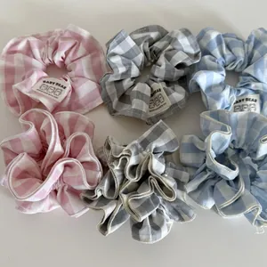 Dettaglio di elastici scrunchie a quadretti con etichette Baby Bear in rosa, grigio e blu