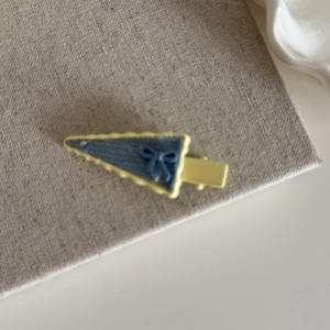 Detail of denim blue triangular hair clip with yellow scalloped edges and blue bow