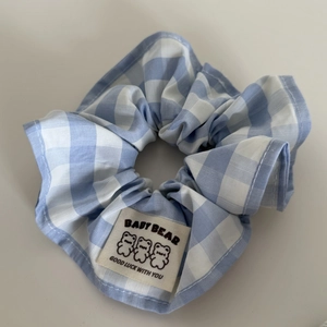 Dettaglio dell'elastico per capelli a scacchi bianchi e blu con etichetta a forma di orso