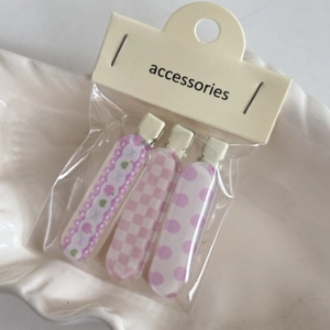 Dettaglio di un set di tre fermagli per capelli rosa con motivi floreali e a quadretti