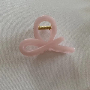 Detail view of pink jelly hair claw clip with golden spring on white textured fabric