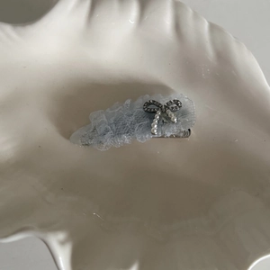 Détail d'une pince à cheveux en dentelle bleu clair avec pendentif perle dans un plat en céramique