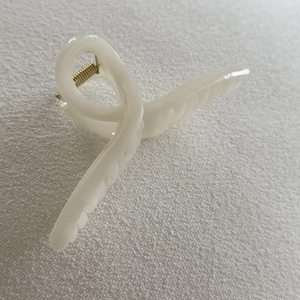 Close-up of a creamy white resin hair claw clip with golden metal spring on fabric