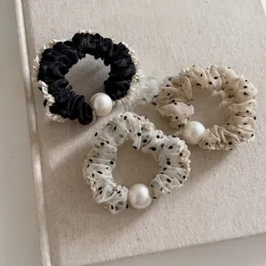 Close-up of three mesh scrunchies featuring black polka dots and elegant white pearls