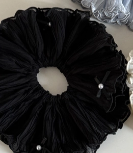Détail d'un chouchou noir oversize avec des nœuds élégants et des perles blanches