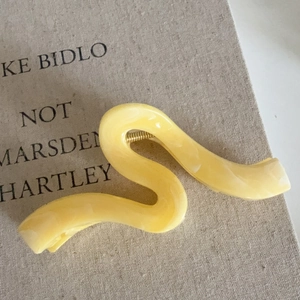 Pince à cheveux en résine jaune crème avec texture marbrée sur fond de livre en lin