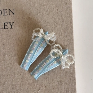 Détail de deux barrettes brodées bleu clair avec des nœuds en perles élégants
