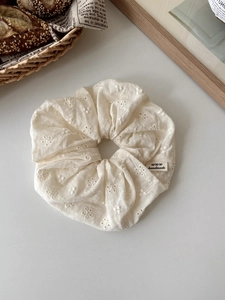 Detailed macro of cream cotton embroidery scrunchie with a black handmade woven label