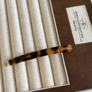 Detail view of handmade tortoiseshell acetate hair clip on a beige jewelry display stand