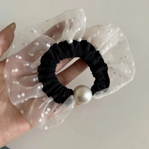 Close-up of a stylish black and white polka dot mesh scrunchie featuring a large faux pearl