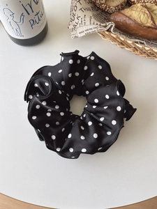 Detailed close-up of a black satin scrunchie with white polka dots in a French retro style