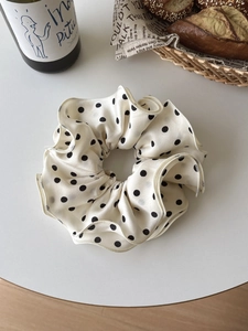 Detail of white satin scrunchie with black polka dots and ruffled edges on a table