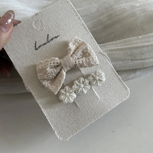 Detailed macro of beige lace bow and embroidered flower hair clips on display card