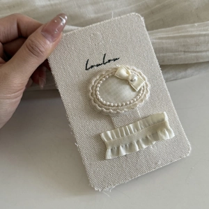 Detail of cream lace hair clips with satin bow and pearl on textured fabric card