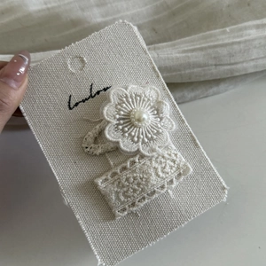Close-up of elegant lace flower hair clip with cream pearl detail on display card