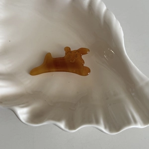 Cute amber acetate dog hair clip displayed on a white shell-shaped ceramic tray