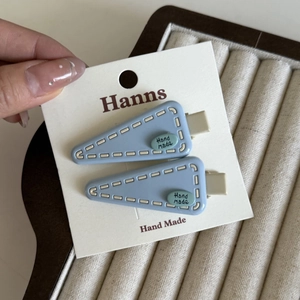 Détail de barrettes bleues en triangle avec couture blanche et logo Hand Made