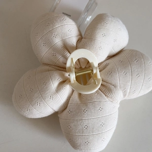 Detail of a large beige floral hair claw clip featuring soft knitted fabric and gold spring