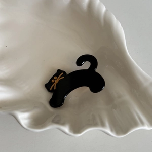 Detail of a black cat acetate hair clip with golden eyes in a white shell dish