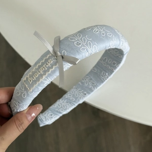 Détail d'un serre-tête bleu clair avec broderie de feuilles blanches et nœud en satin