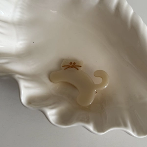 Detailed close-up of a cute cream-colored acetate cat hair clip on a white shell tray