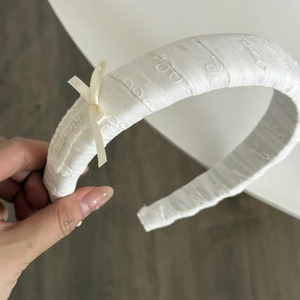 Détail d'un serre-tête blanc avec broderie florale et petit nœud en ruban de soie beige