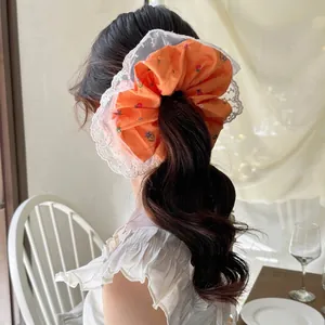 Orange floral scrunchie with lace trim shown on a ponytail in a cozy indoor setting