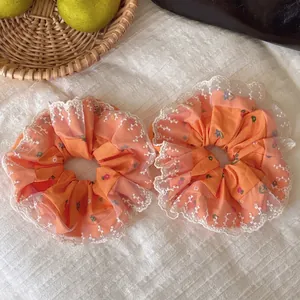 Set of two orange floral hair scrunchies with white lace trim on white tablecloth