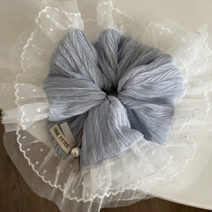Détail d'un chouchou plissé bleu clair avec dentelle blanche, nœud gris et perle