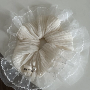 Gros plan d'un chouchou blanc en dentelle avec mesh à pois, nœud et détail perle