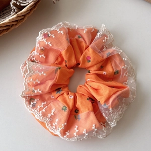 Close-up of orange floral hair scrunchie with delicate white lace edging and embroidery