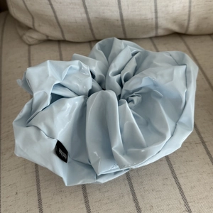 Detail of light blue glossy leather scrunchie with a black Hand Made fabric label