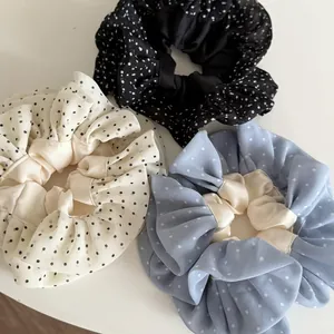 Close-up of three dotted scrunchies in black, cream, and light blue silk-like fabric