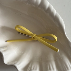 Macro shot of a yellow leather bow hair clip on a white seashell ceramic plate
