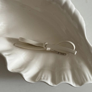 Elegant cream PU leather bow hair clip placed on a textured ceramic white plate