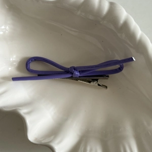 Detail view of a purple bow hair clip made of synthetic leather on a white shell tray